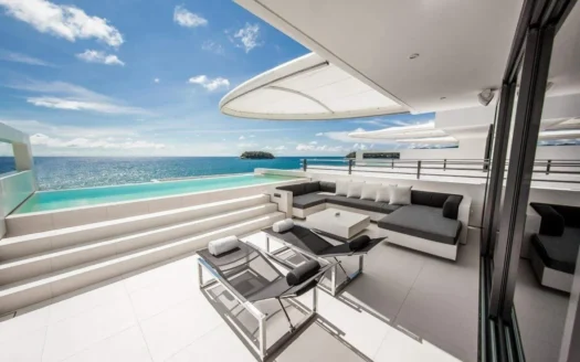 Освещенная солнцем терраса с белой мебелью у бассейна и океана