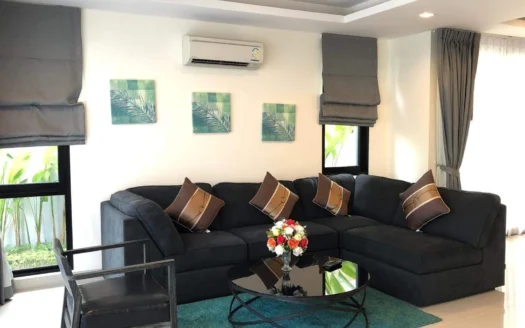 Уютный темный диван в светлой гостиной с картинами пальмами