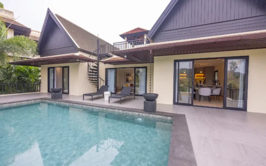 Открытый бассейн рядом с современной бежевой виллой с темной крышей