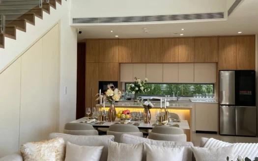 Гостиная открытой планировки с бежевым диваном и обеденным столом, кухня на заднем плане