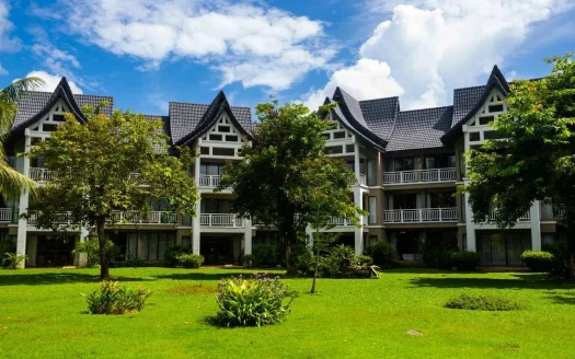 Внешний вид отеля в балийском стиле на зелёном газоне и деревьях