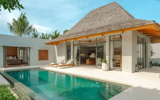 Вилла с соломенной крышей, стеклянными стенами и шезлонгами у бассейна