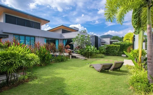 Солнечный современный сад виллы с двумя шезлонгами и тропическими растениями
