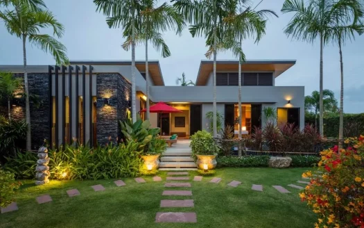 Современный фасад дома с пальмами и тепло освещённой садовой дорожкой