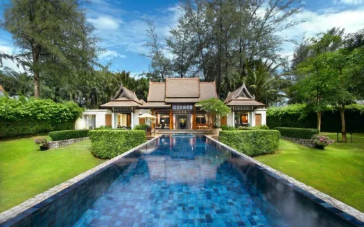 Уличный вид тропической виллы с длинным синим бассейном и соломенными беседками