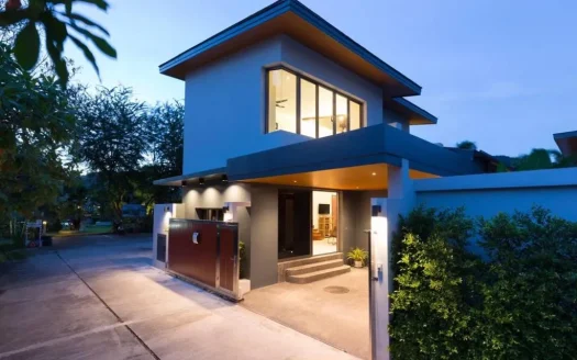 Современный двухэтажный дом с подсветкой входа и воротами на подъезде в сумерках