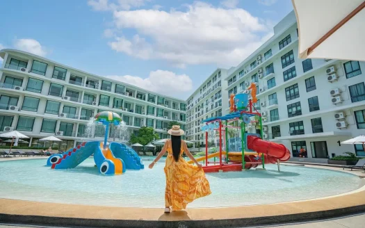 Женщина в желтом платье стоит у края бассейна рядом с водной площадкой