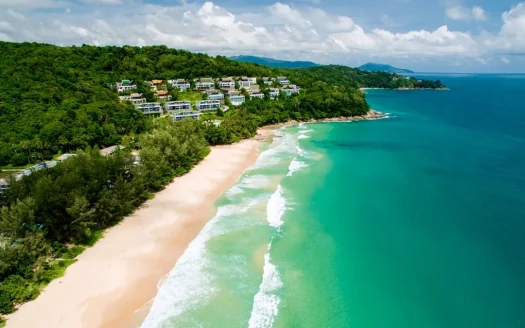 Аэросъемка песчаного пляжа с бирюзовой водой и домами на склоне холма