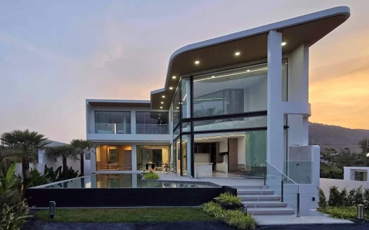 Двухэтажный современный дом с изогнутой крышей и стеклянным фасадом на закате